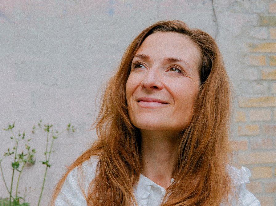 Iben Maria Zeuthen foran en murstensvæg. Hun kigger op og smiler. 